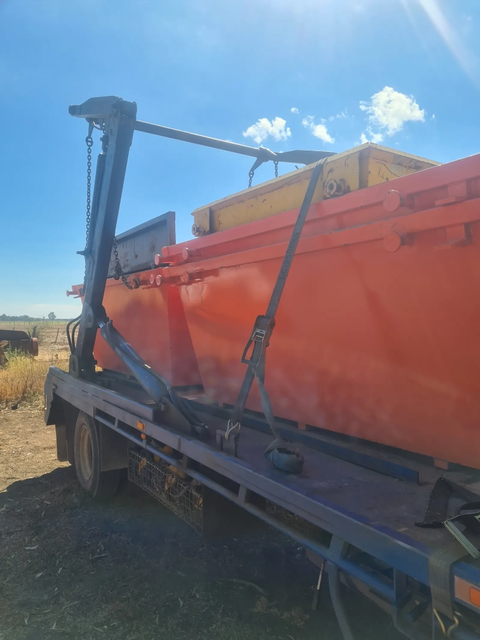 Skip-lift truck with a skip bin strapped down